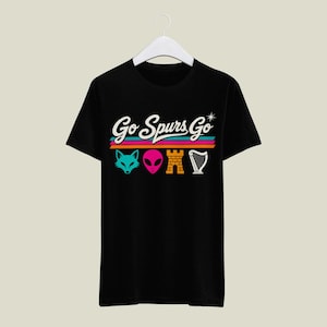 K&ouml;nnte beinhalten: Schwarzes T-Shirt mit dem Schriftzug "Go Spurs Go" in wei&szlig; &uuml;ber bunten horizontalen Streifen. Darunter befinden sich vier farbige Symbole: ein t&uuml;rkisfarbener Fuchskopf, ein rosa Alienkopf, eine gelbe Burg und eine wei&szlig;e Harfe.