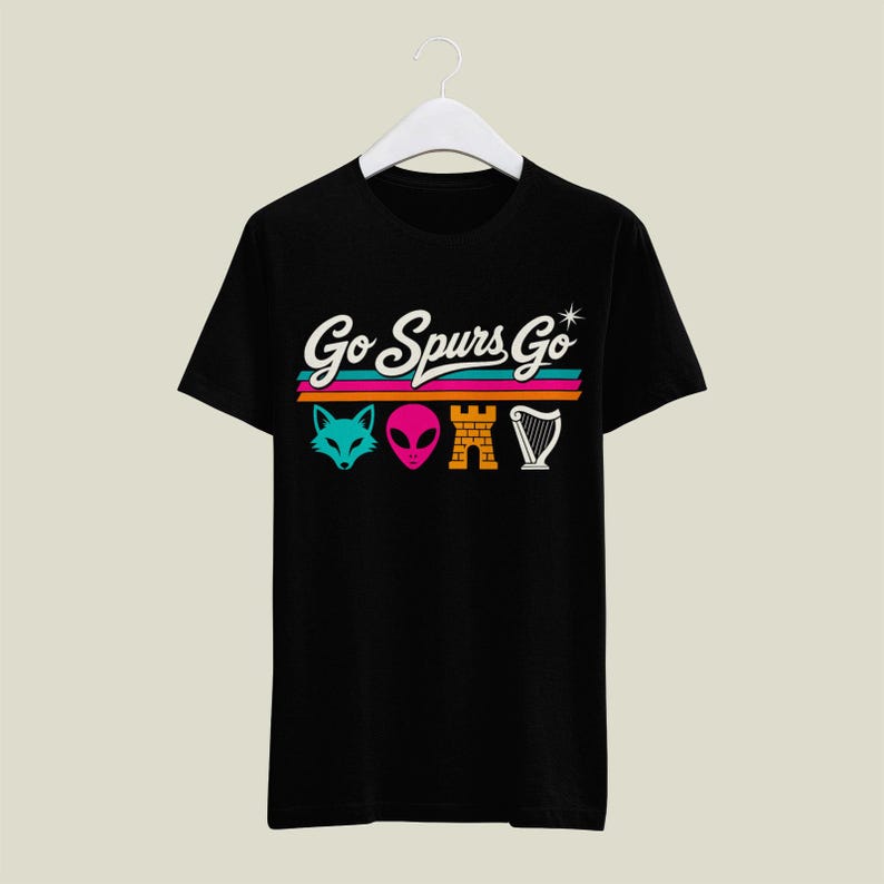 K&ouml;nnte beinhalten: Schwarzes T-Shirt mit dem Schriftzug "Go Spurs Go" in wei&szlig; &uuml;ber bunten horizontalen Streifen. Darunter befinden sich vier farbige Symbole: ein t&uuml;rkisfarbener Fuchskopf, ein rosa Alienkopf, eine gelbe Burg und eine wei&szlig;e Harfe.