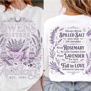 May include: A white t-shirt featuring purple graphic prints. The front displays a mortar and pestle, lavender, and the text "OWENS SISTERS APOTHECARY EST. 1995". The back features lavender sprigs, a salt shaker, and text about salt, rosemary, and lavender.