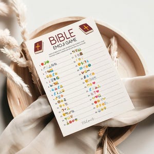 May include: A printed game sheet titled "BIBLE EMOJI GAME" with a cross and book graphic. The game sheet features a series of emoji-based clues. The sheet is on a wooden tray with decorative elements.