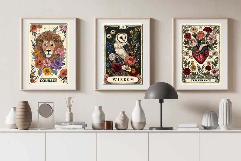 K&ouml;nnte beinhalten: Drei gerahmte Drucke mit floralen Designs und Tarotkarten-Bildern. Der erste Druck zeigt einen L&ouml;wenkopf mit dem Wort "MUT" darunter. Der zweite Druck zeigt eine Eule mit dem Wort "WEISHEIT" darunter. Der dritte Druck zeigt ein Herz mit dem Wort "M&Auml;SSIGKEIT" darunter.