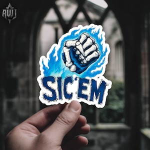 May include: A sticker featuring a stylized illustration of a skeletal hand clenching a fist, surrounded by blue flames. The word "SIC'EM" is written in bold, blue letters below the hand. The sticker is held by a hand.