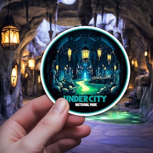Könnte beinhalten: Ein runder Aufkleber mit einer grünen, blauen und schwarzen Illustration einer Höhle mit leuchtenden Lichtern und einem Fluss. Der Aufkleber lautet "Undercity National Park".