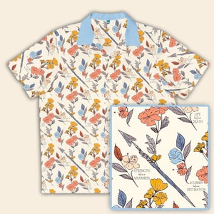 Può includere: Una camicia bianca a maniche corte con bottoni e un motivo floreale. La camicia ha un colletto blu chiaro e una tasca sul lato sinistro. Il motivo include fiori, frecce e il testo "Life before Death", "Strength before Weakness" e "Journey before Destination".