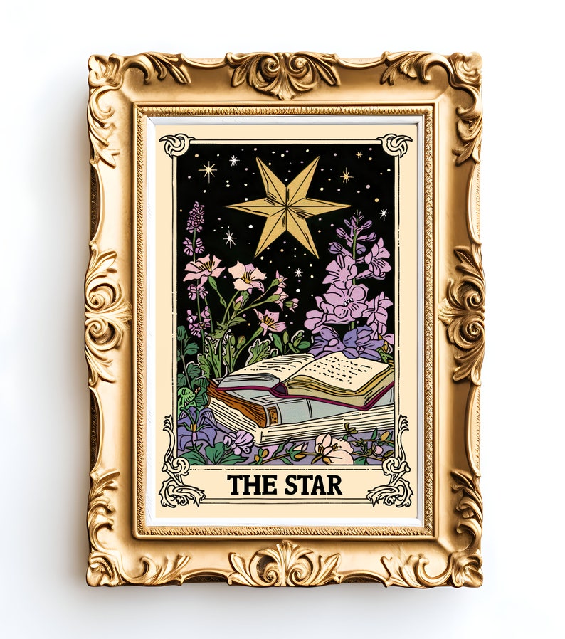May include: A gold framed print of a tarot card depicting The Star. The card features a large, five-pointed star with a yellow outline and a black interior. The star is surrounded by a dark blue background with small white stars. The card also features a book with a red spine and a few flowers in purple, pink, and white.