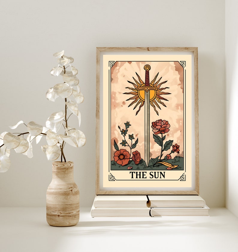 May include: A vintage-style tarot card illustration of The Sun card. The card features a sword piercing a sun with rays, surrounded by flowers. The card is framed in a wooden frame and has a beige background.