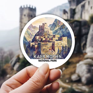 May include: A white round sticker with a watercolor illustration of a medieval castle in a mountain valley. The text "Kaer Morhen National Park" is printed in black at the bottom of the sticker.