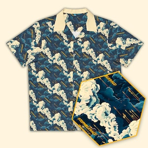 May include: A blue and white short-sleeved button-up shirt with a cloud and arrow pattern. The shirt has a yellow collar and a yellow pocket on the left side. The text "Stormblessed" and "Blessed" is printed on the shirt.