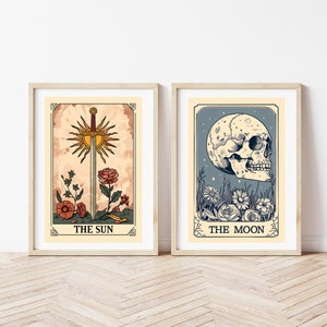 May include: Two framed tarot card prints, one depicting The Sun with a sword and flowers, the other depicting The Moon with a skull and flowers.