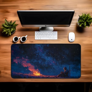 May include: A rectangular mouse pad featuring a digital painting of a knight sitting near a campfire under a starry sky. The pad has a black border and is placed on a wooden desk with a computer, keyboard, mouse, and coffee cups.