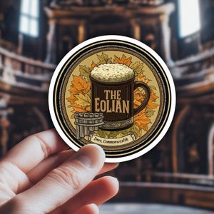 May include: A round sticker featuring a dark brown mug of beer with the text "THE EOLIAN". The mug is surrounded by autumn leaves and a small barrel. The text "Imre, Commonwealth" is at the bottom.