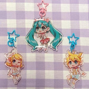 Peut inclure: Trois porte-clés de personnages d'anime colorés avec des accents de paillettes. Chaque porte-clés présente un personnage différent avec des accents bleus, roses et jaunes. Les porte-clés sont attachés à des breloques en forme d'étoile bleue et rose.