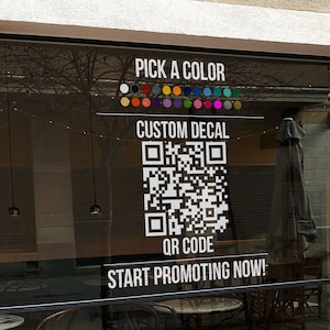 May include: A white QR code decal with the text "CUSTOM DECAL" and "QR CODE" on a storefront window. The decal also includes the text "START PROMOTING NOW!" and "CONTACT US FOR ANY QUESTIONS OR DESIGN HELP. GRAPHIC DESIGNERS AVAILABLE FOR HELP!"  The decal has a color selection guide with 16 different color options.
