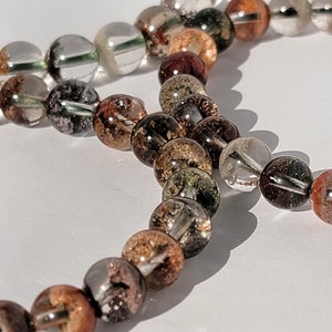 May include: A multi-colored beaded bracelet with brown, green, and clear beads. The beads are round and have a translucent appearance.
