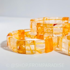 Könnte beinhalten: Zwei übereinanderliegende Armbänder aus durchsichtigen und gelben quadratischen Perlen. Die Perlen haben eine durchscheinende, wolkige Optik mit einem dezenten goldenen Farbton.
