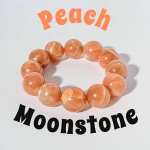 May include: Peach Moonstone bracelet. The image shows a bracelet made of peach-colored, spherical moonstone beads. The beads are strung together to form a circular shape. The word "peach" is written in orange script above the bracelet, and the word "Moonstone" is written in black script below.