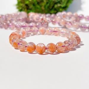 May include: A beaded bracelet featuring translucent, round beads in shades of orange, pink, and white. The bracelet is made of multiple beads strung together, with a second bracelet visible in the background. The beads have a marbled appearance.