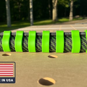 Op de afbeelding: Een close-up van een kabelmanagementsysteem met een zwart-groene gevlochten kabel, vastgezet met felgroene clips. De afbeelding bevat een kleine Amerikaanse vlag en de tekst "MADE IN USA".