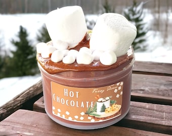 Könnte beinhalten: Ein transparentes Glasgefäß gefüllt mit braunem Schokoladenschleim, der mit weißen Marshmallows bedeckt ist. Das Gefäß trägt ein Etikett mit der Aufschrift "Hot Chocolate" und "Fuzzy Slime".