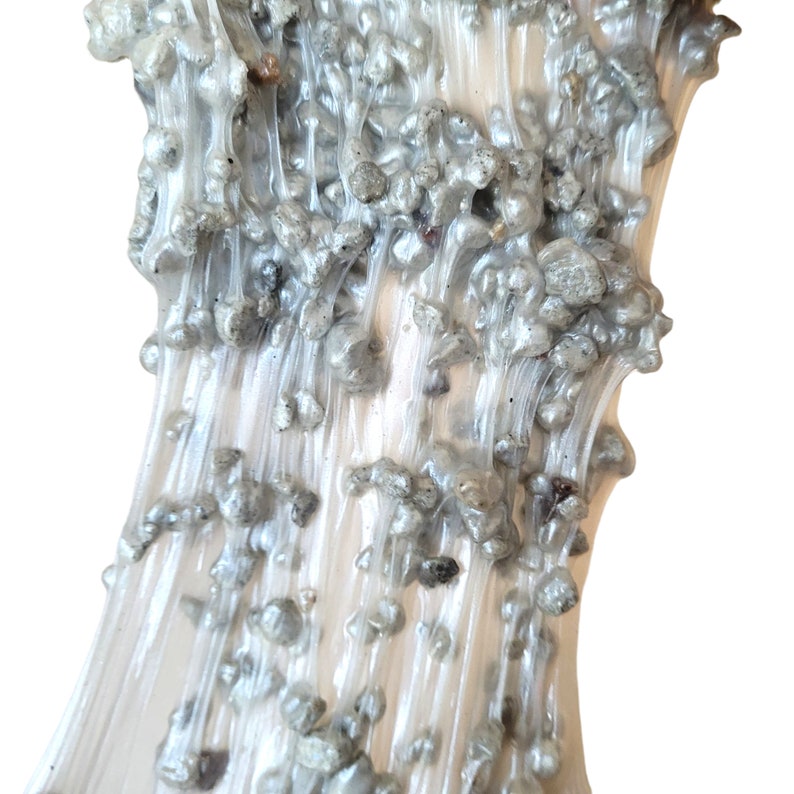 May include: Close-up of clear slime with silver glitter embedded throughout. The slime is stretched and flowing, creating a textured, abstract pattern.