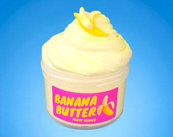 Könnte beinhalten: Ein gelber, fluffiger Schleim in einem durchsichtigen Plastikbehälter mit einem rosa Etikett, auf dem "Banana Butter Fuzzy Slime" steht. Der Schleim ist mit einer gelben Bananenscheibe bedeckt.