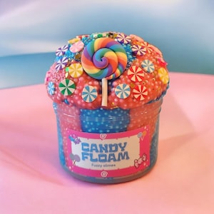 May include: A jar of "Candy Floam" fuzzy slime, featuring a vibrant rainbow lollipop and colorful candy decorations. The slime is pink and blue, with a label that reads "Candy Floam" and "Fuzzy slimes".