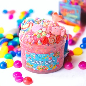 May include: Pink slime with candy sprinkles, lollipops, and a candy cane. The slime is in a clear jar with a blue label that says "Candy Shop" and "Fuzzy Slimes".