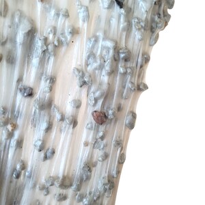 May include: Close-up of a white, translucent substance with small, gray, pebble-like inclusions. The substance has a flowing, stringy texture.