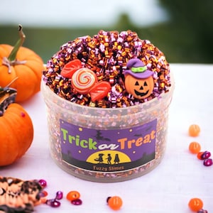 May include: A clear plastic container filled with orange and purple glitter slime with a Halloween theme. The slime is topped with a candy cane, a red heart, and a small pumpkin with a witch's hat. The container has a purple label that says "Trick or Treat" and "Fuzzy Slimes".