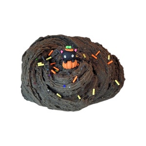 Puede incluir: Slime negro con chispas naranjas y amarillas y una figurita de gato negro sentada en una calabaza.