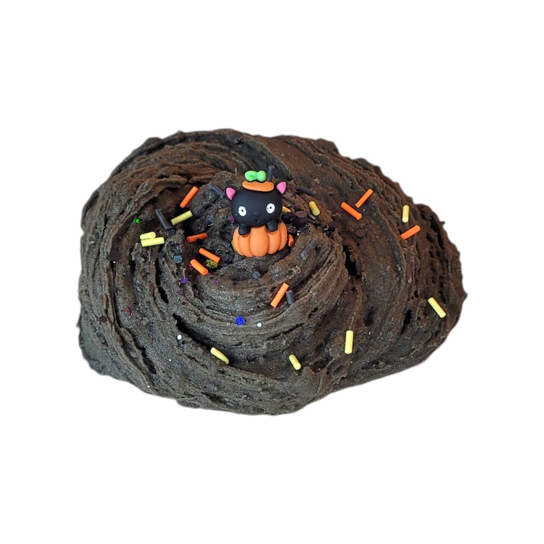 Puede incluir: Slime negro con chispas naranjas y amarillas y una figurita de gato negro sentada en una calabaza.