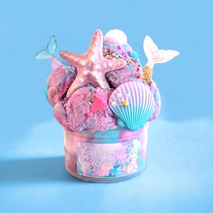 May include: A jar of Mermaid Ice Cream with a colorful, textured appearance. The ice cream is topped with a pink starfish, a seashell, and mermaid tail decorations. The jar has a label that reads "Mermaid Ice Cream."