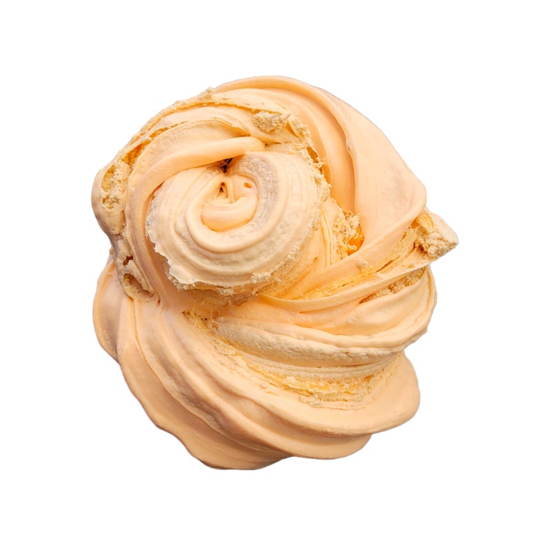 May include: A close-up shot of a swirl of light orange-colored slime, with a creamy texture. The slime is in a rounded shape, with a spiral in the center. The background is plain white.