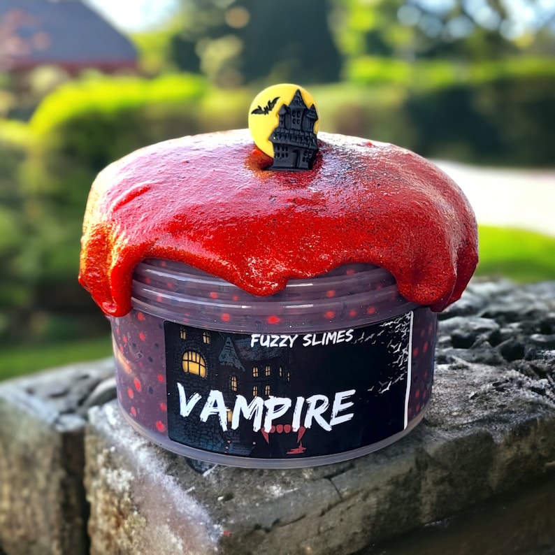 K&ouml;nnte beinhalten: Ein roter Schleim mit einem schwarz-wei&szlig;en Etikett, auf dem "Fuzzy Slimes Vampire" steht. Der Schleim befindet sich in einem durchsichtigen Beh&auml;lter und hat einen schwarzen und gelben Haus-Anh&auml;nger oben drauf.