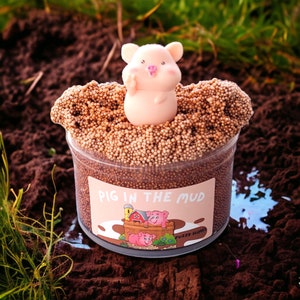 May include: A brown slime with a pig figurine on top. The slime is in a clear container with a label that says "Pig in the Mud" and "Fuzzy Slime".