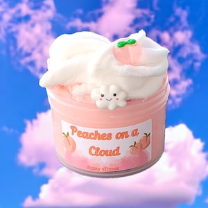 May include: A pink and white slime with a peach-shaped charm and a cloud charm. The slime is in a clear jar with a label that says "Peaches on a Cloud" and "fuzzy slimes".