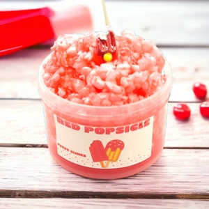 May include: A clear plastic container filled with red, fluffy slime. The container has a white label that says "Red Popsicle" and "Fuzzy Slime".