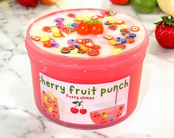 Könnte beinhalten: Ein rosa Behälter mit "Cherry Fruit Punch" Fuzzy-Schleim, verziert mit fruchtförmigen Streuseln und zwei kirschförmigen Dekorationen. Das Etikett zeigt eine Kirschenillustration und die Worte "fuzzy slimes".