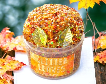 Könnte beinhalten: Ein durchsichtiger Behälter gefüllt mit braunem, orangefarbenem und goldenem Glitzer-Schleim mit einem Etikett mit der Aufschrift "Glitter Leaves" und "Fuzzyslimes".