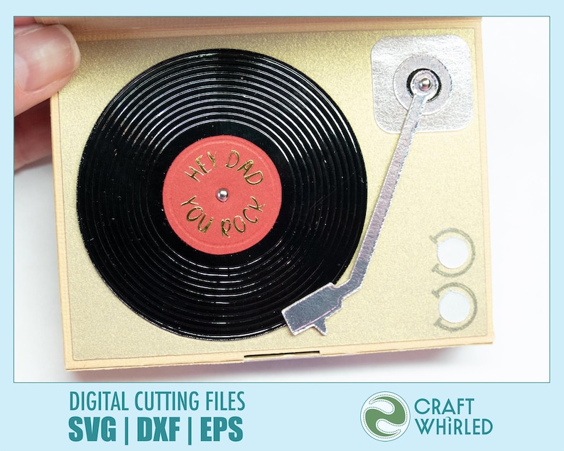 Puede incluir: Una tarjeta dorada con forma de tocadiscos vintage. El disco negro tiene el texto "Hey Dad You Rock" en una etiqueta roja. La tarjeta tiene un brazo plateado y dos botones circulares. La tarjeta est&aacute; sujeta por una mano.