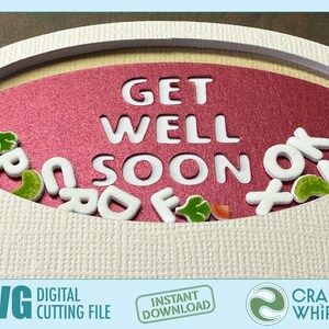 Op de afbeelding: Een roze ovale kaart met de woorden "Get Well Soon" uitgesneden. Witte schuimletters zijn rond de kaart verspreid, samen met groene en oranje viltvormen.