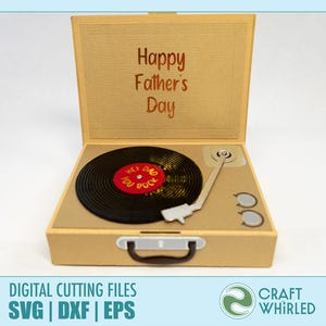 Puede incluir: Una caja beige abierta que se asemeja a un tocadiscos vintage, con las palabras "Happy Father's Day" en la cubierta interior. Un disco de vinilo negro con detalles en rojo y amarillo est&aacute; en el tocadiscos. El texto "HEY DAD YOU ROCK" est&aacute; en el disco.