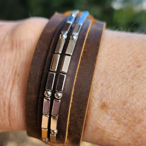 May include: A brown leather bracelet with a silver metal chain and beads. The bracelet is worn on a person's wrist.