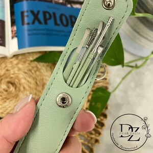 May include: A sage green leather case with a snap closure, containing a set of six silver tools. The case has the text "Dear Zalia Handmade Personalised" on the bottom.