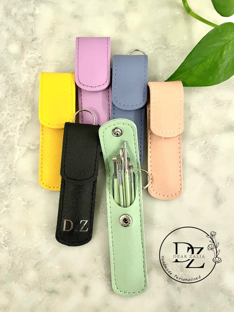 May include: Six different colored leather pouches with a silver keychain. The pouches are lined up in a row. The pouch in the center is open and contains a set of small tools. The pouch is light green and has the initials "D.Z." on it. The other pouches are yellow, black, purple, blue, and pink.