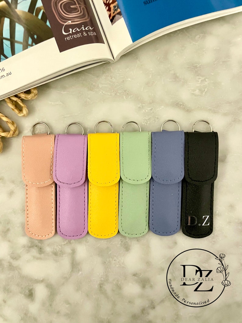 May include: Seven colorful leather keychains with silver rings. The keychains are in shades of pink, purple, yellow, green, blue, and black. The black keychain has the initials "D.Z." embossed on it.