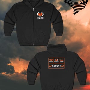 May include: Black zippered hoodie with a white logo that says "Skywarn" and an orange eye graphic. The back of the hoodie has a white graphic with the words "Monitor, Observe, Report" and "Repeat" in a box.