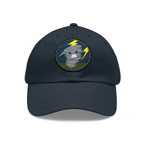 May include: A navy blue baseball cap with a patch featuring a cartoon tornado with a lightning bolt and angry face.
