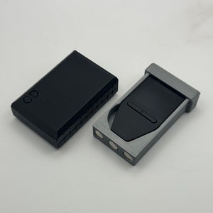 May include: A black case with the letter "CD" on it and a gray case with a black device inside. The device has a small button on the top.