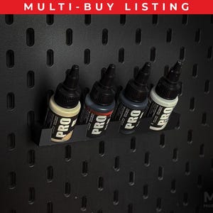 May include: A black pegboard displaying four paint bottles in a black holder. The bottles are labelled "PRO" and contain beige, red, and grey paint. The text "MULTI-BUY LISTING" is at the top.